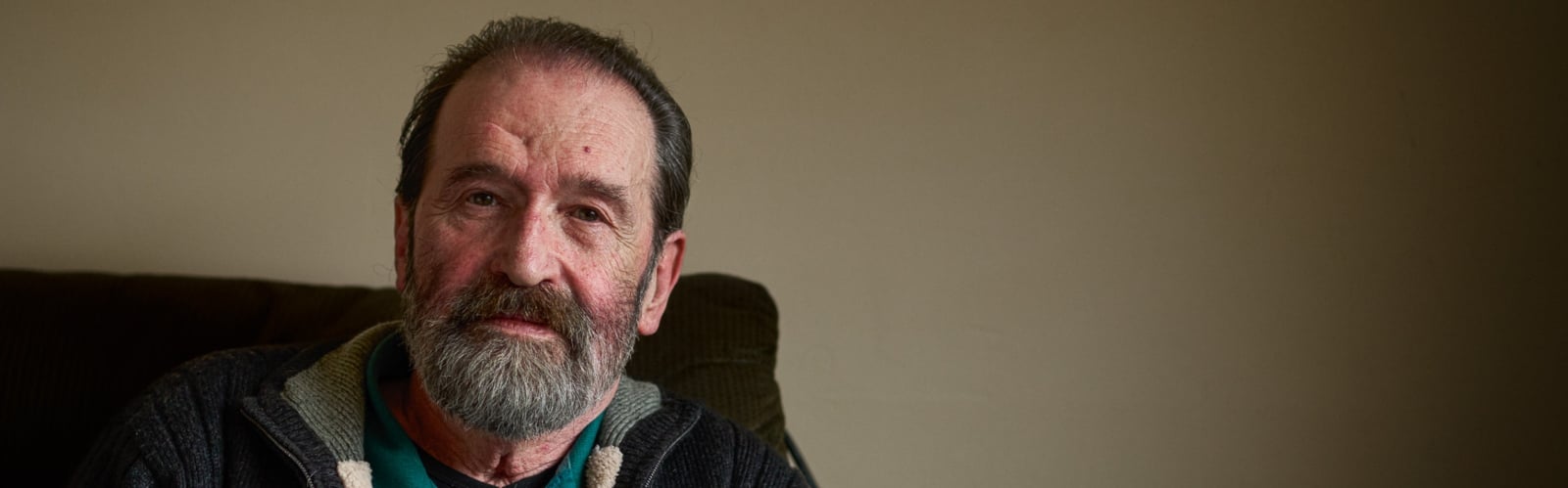 An older man with a beard stares sadly at the camera